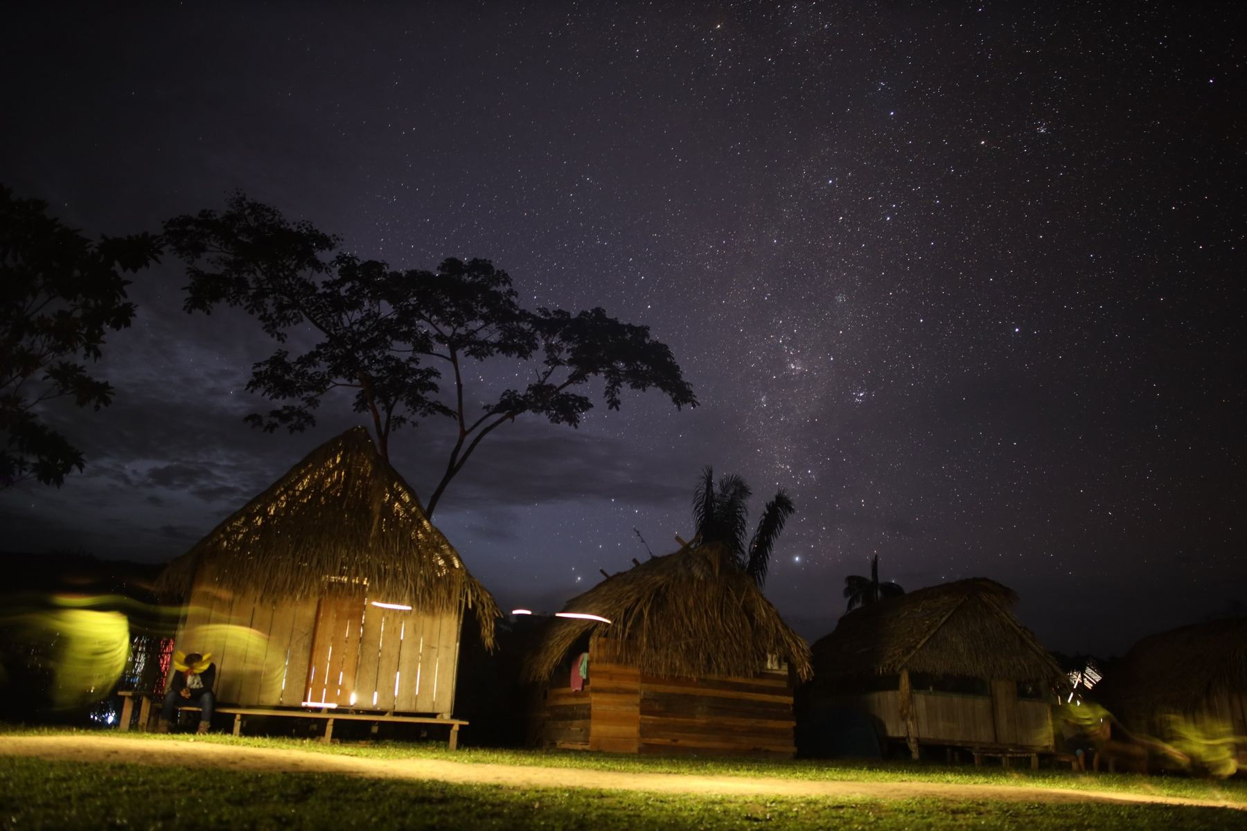 Thatched wooden houses at night under a sky full of stars and the Milky Way