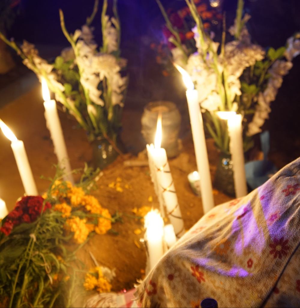 Cempasúchil flowers and lit candles on a grave at night in Huautla